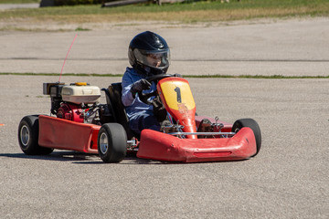 Boy with black helmet driving a red go kart outdoors