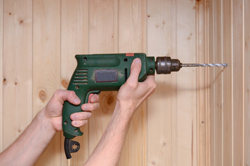 Hands hold an old drill with a drill and drill a wooden wall