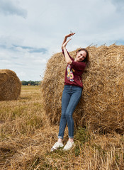 young girl having fun in the field, mowed hay wrapped in a haystack