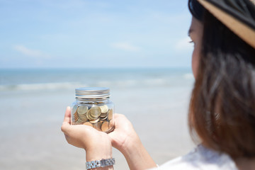 Woman holding gold coins money in bottle on sea and beach background, Growth for the save money concept.