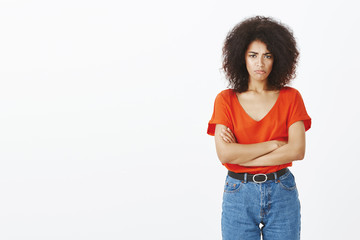 Studio shot of gloomy offended attractive curly-haired woman with dark skin, sulking holding hands...
