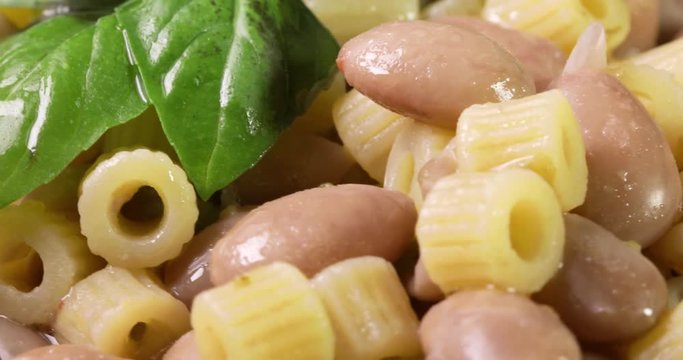 Italiana Pasta ditalini rigati e fagioli con foglie di basilico fresco e olio extra vergine di oliva su un piatto bianco isolato. Dieta Mediterranea. Vista macro.