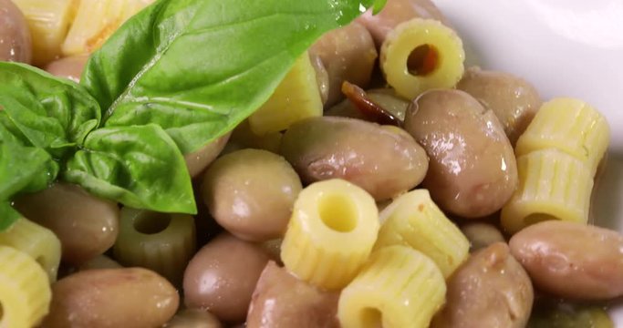 Italiana Pasta ditalini rigati e fagioli con foglie di basilico fresco e olio extra vergine di oliva su un piatto bianco isolato. Dieta Mediterranea. Vista macro.