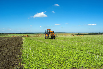 self-propelled sprayer works on a field under a blue sky with clouds