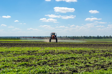 self-propelled sprayer works on a field under a blue sky with clouds