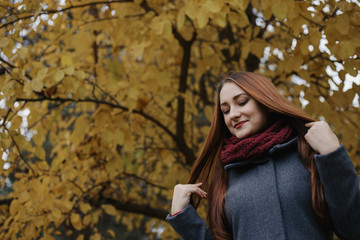The girl touching hair. Young romantic female person wearing warm grey overcoat and red scarf....