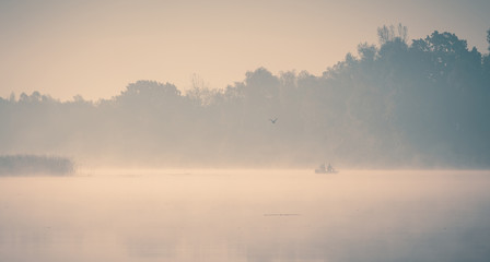 Foggy river at beautiful early autumn morning. Fishermans in the rubber boats and seagull flying over.
