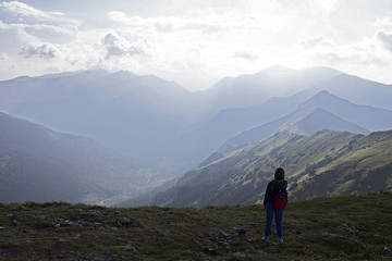 A young woman is standing with her back on a mountains background.