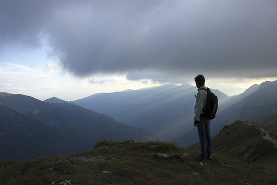 A male mountaineer looking over a vast, rocky, mountainous sunrise scene.