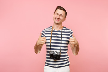 Fototapeta premium Portrait of smiling young photographer man wearing striped t-shirt take pictures on retro vintage photo camera isolated on trending pastel pink background. People sincere emotions lifestyle concept.
