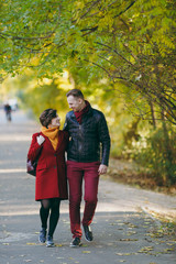 Fototapeta premium Young loving couple, smiling woman and happy man in casual warm clothes walking, embracing and looking at each other on road in autumn city park outdoors. Love relationship family lifestyle concept.