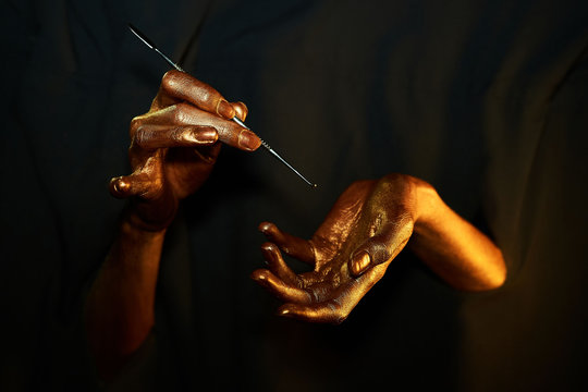 two golden hands with a dental instrument on a black background