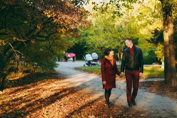 Obraz premium Young happy beautiful couple in love smiling woman and man in casual warm clothes walking by hands on road in autumn city park outdoors in sunny day. Love relationship family people lifestyle concept.