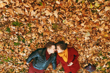 Top side view of young happy beautiful couple in love woman and man with closed eyes facing each other lying on fallen leaves in autumn city park outdoors. Love relationship family lifestyle concept.