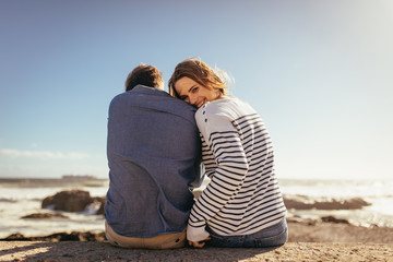 Couple sitting on a sea wall together - obrazy, fototapety, plakaty
