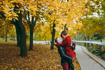 Young couple in love handsome man holding woman in his arms embracing hugging looking at each other on walk near water in autumn city park outdoors. Love relationship family people lifestyle concept.