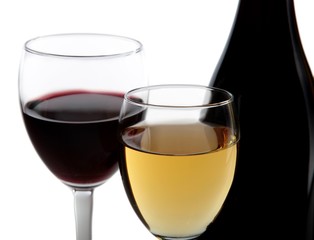 A glass of white wine and a glass of red wine next to bottles of
