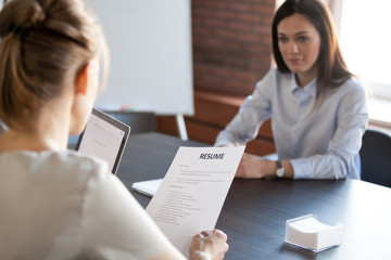 Back close up view of female employer holding applicant resume during office interview, millennial...
