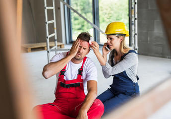 A woman with smartphone helping man worker after an accident at the construction site.