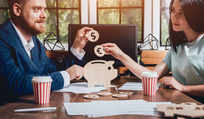 A businessman with a bank employee holds a coins under a wooden pig. Money box. Collecting money with earning bank.