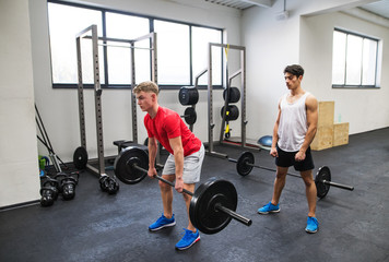Fit young men in gym working out, lifting barbell.