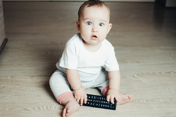 The baby plays with the TV remote sitting on the floor