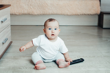 The baby plays with the TV remote sitting on the floor