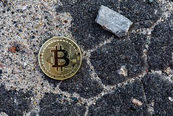 lonely bitcoin coin thrown on asphalt road next to a large stone