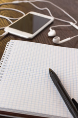 Business concept: Notepad and pen. Phone with headphones on the table. Close-up