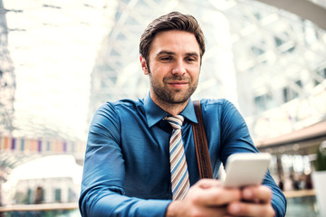 A young businessman with smartphone standing in a modern building, texting.