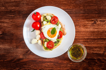 Sandwich toasts with agg, tomatoes cherry, mozzarella, avocado, basil and olive oil. Top view on a dark wooden background. Flat lay.