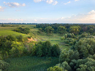 Obraz premium Aerial view from the drone of a natural landscape with greenery, forest, field, ravine on a background of a cloudy sky.