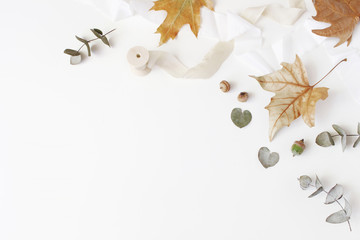 Fall creative styled composition. Autumn floral arrangement with dry eucalyptus, maple leaves and silk ribbon on white table background. Feminine flat lay, top view. Empty space.