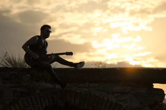 Man performs on electric guitar on old Roman aqueduct during sunset. © dragan.ristovski