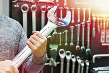 Big wrench in hands near wall with tools in store