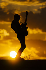 Man performs on electric guitar on old Roman aqueduct during sunset.