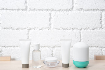 Different cosmetic products on table against brick wall