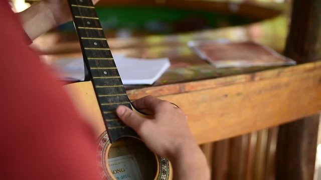 Man learning how to play on old classic guitar, sitting outside. Close-up of his fingers and strings.