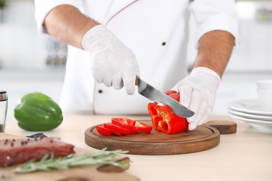 Professional chef cutting pepper on table in kitchen, closeup