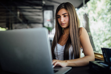 Naklejka premium Beautiful woman dreaming about something while sitting with portable net-book in modern cafe bar. Young charming female freelancer thinking about new ideas during work on laptop computer