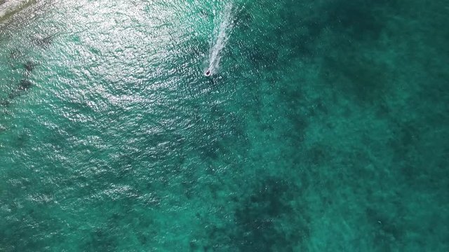 Overhead aerial, boat travels on tropical water