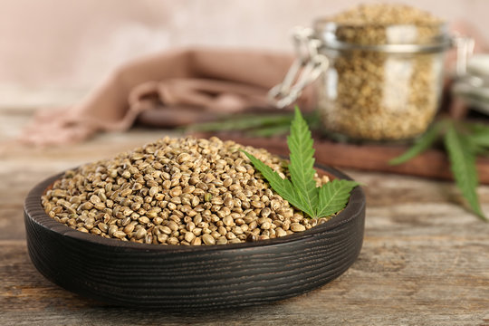 Bowl of hemp seeds on wooden table against color background