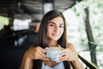 Young woman sitting alone in a terrace at cafe outdoor and drinking a cup of tea