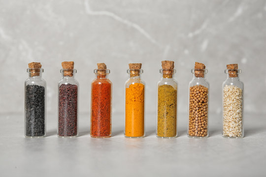 Row of small glass bottles with different spices on color background