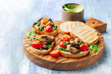 Delicious bruschetta with tomatoes and mushrooms on cutting board on the table 