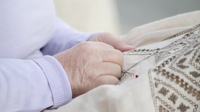 Senior woman doing needlework and decorating textile with embroidery patterns