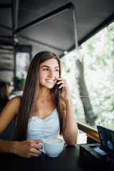 Young woman talking on a phone and drinking coffee in a cafe. Coffee time.