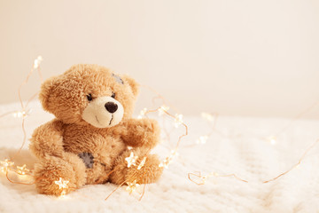 Toy teddy bear on soft plaid background with beautiful Christmas lights. Winter time, holiday, gift...