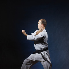 Adult athlete performs formal karate exercises in white karategi