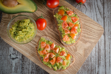 Avocado toast, cherry tomato and poached eggs on wooden background. Breakfast with vegetarian food, healthy diet concept.